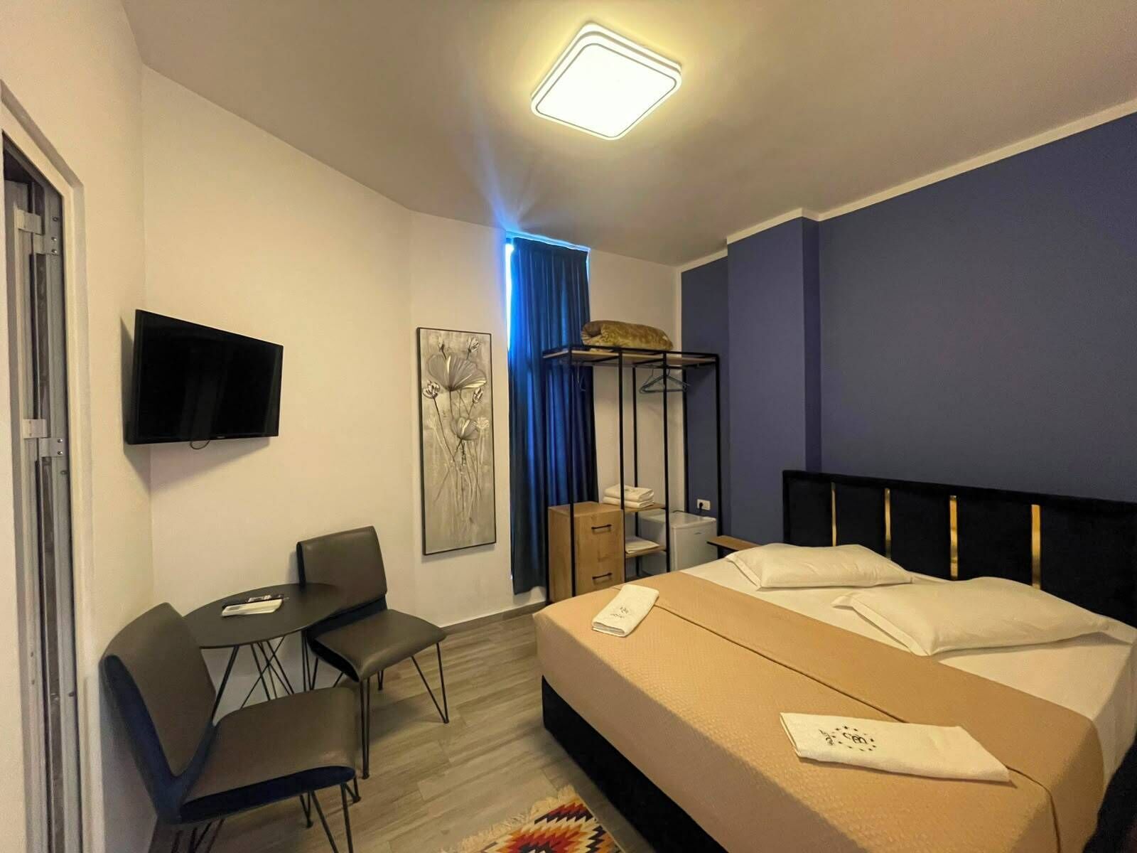 Hotellihuone, jossa on sänky, työpöytä, tuoli, televisio ja taulu seinällä.