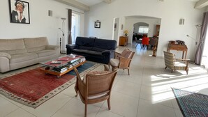 A spacious living room with a sofa, a coffee table with books, and a dining area with chairs and a table. - 5 kms from Aix en Provence (Puyricard) 4-bedroom villa swimming pool garden 2000 m2 (Aix-en-Provence)