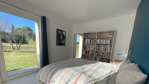 A bedroom with a large window, a bed with a patterned bedspread, a bookshelf, and a painting on the wall. - 5 kms from Aix en Provence (Puyricard) 4-bedroom villa swimming pool garden 2000 m2 (Aix-en-Provence)