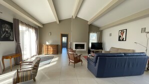 A spacious living room with a large blue sofa, a wooden cabinet, and a television. - 5 kms from Aix en Provence (Puyricard) 4-bedroom villa swimming pool garden 2000 m2 (Aix-en-Provence)