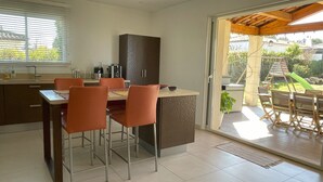A modern kitchen with a dining area, featuring a large island, bar stools, and a sliding glass door leading to an outdoor patio. - 5 kms from Aix en Provence (Puyricard) 4-bedroom villa swimming pool garden 2000 m2 (Aix-en-Provence)