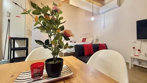 Un salón moderno con techo de madera, una mesa de comedor con planta en maceta y una cama con almohadones rojos y negros.