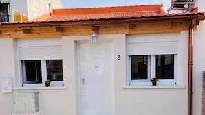 Un edificio con una puerta blanca, dos ventanas con contraventanas y el número 8 en la pared.