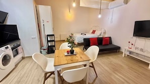 Un espacio habitable compacto con comedor, cama, televisor y lavadora.