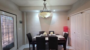 Un comedor con una mesa rectangular, seis sillas, una araña y un dispensador de agua.