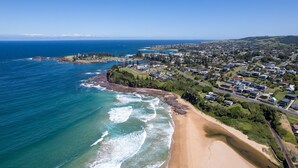 An aerial view of a coastal town with a beach, residential areas, and a lighthouse.