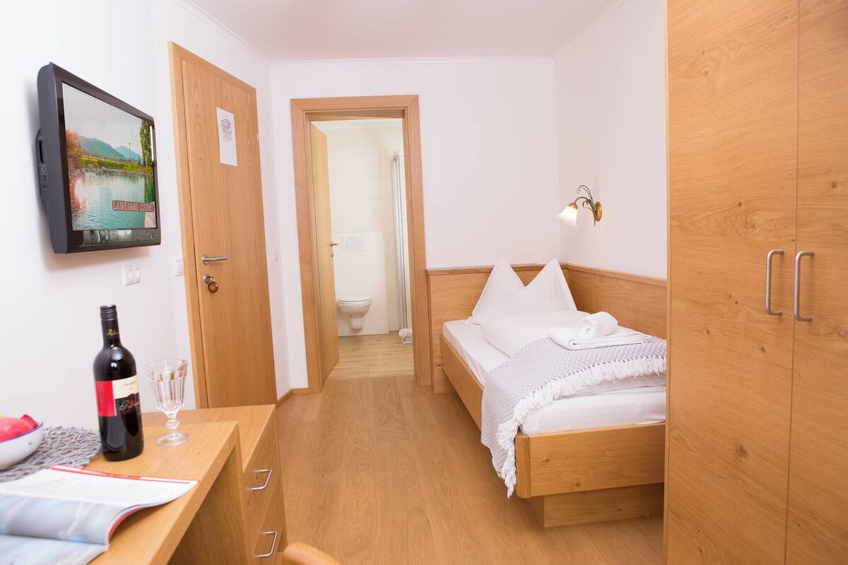 A bedroom with a wooden bed, a desk with a wine bottle, and a TV displaying a scenic image.
