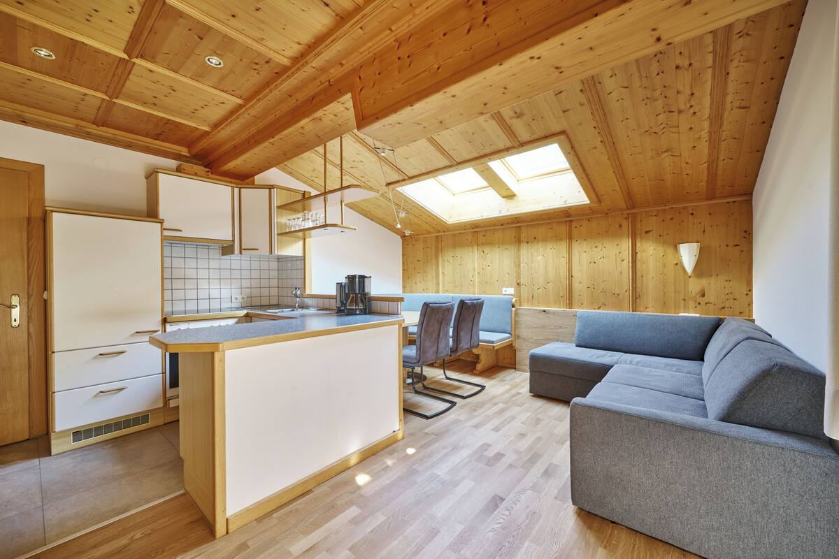 A modern kitchen with wooden beams, a dining area with a sofa, and a skylight.