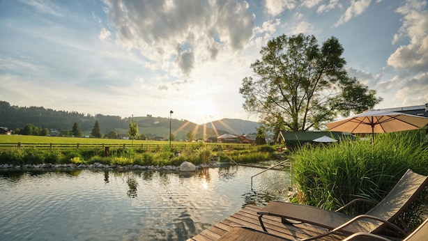 A wooden deck with lounge chairs overlooking a pond, surrounded by greenery and a clear sky. - Landhaus Huber (Altenmarkt im Pongau)