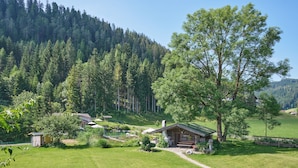 A lodge with a wooden cabin, surrounded by a lush green landscape and a forested hill. - Landhaus Huber (Altenmarkt im Pongau)