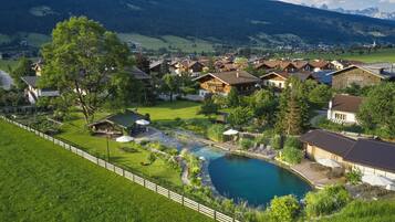 A lakeside property with a swimming pool, wooden cabins, and a view of the surrounding mountains.