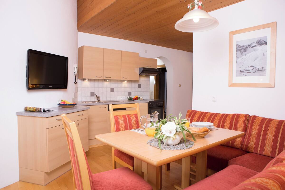 A compact kitchen with wooden cabinets, a black stove, and a dining area with a wooden table and red upholstered seating.