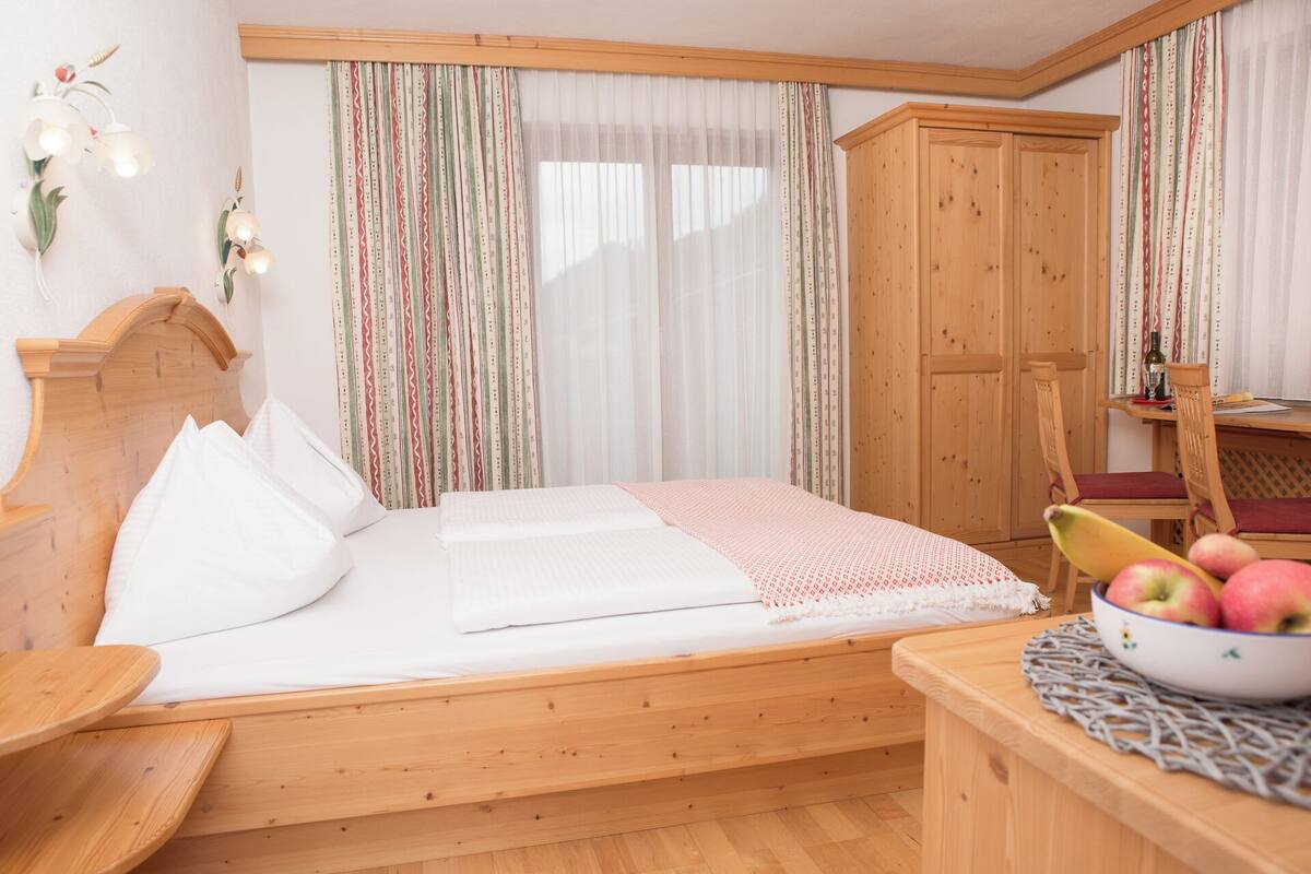 A wooden bed with white bedding, a wooden wardrobe, and a table with a bowl of fruit.
