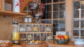 A kitchen with wooden cabinets, a rooster decoration, a bread loaf, a fruit bowl, and a glass of orange juice. - Landhaus Huber (Altenmarkt im Pongau)