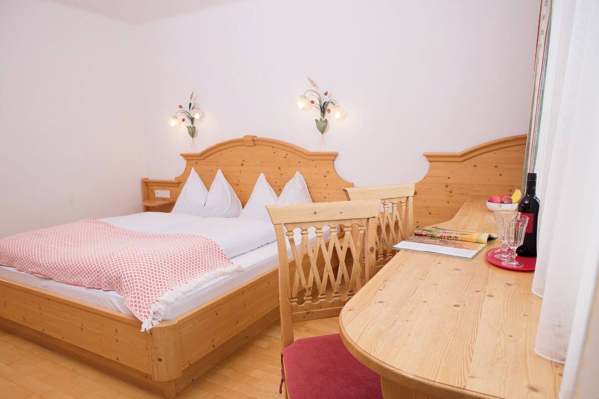 A bedroom with a wooden bed, a small table with a book, a bottle, and a glass.