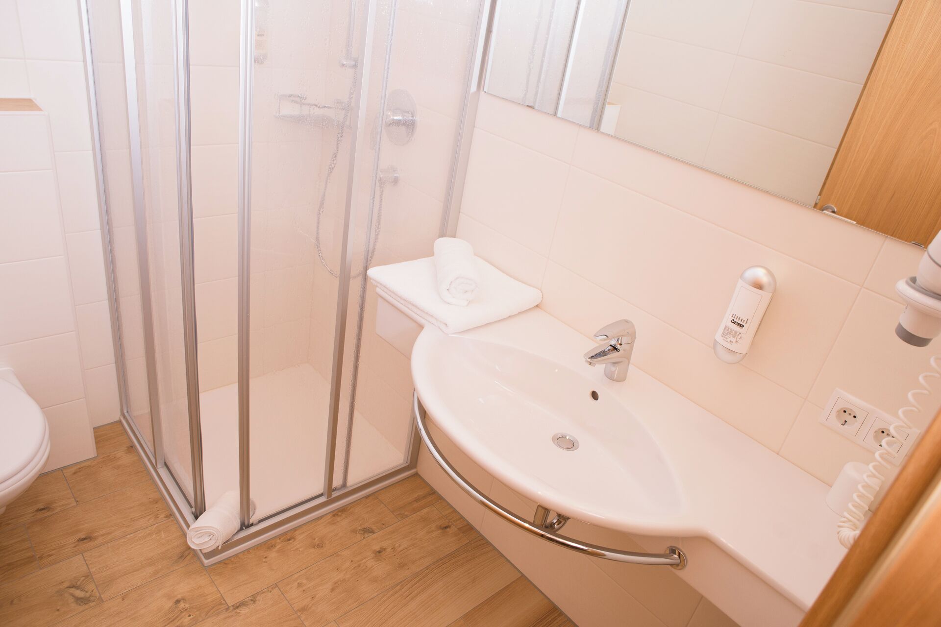 A bathroom with a glass shower enclosure, a white sink with a handheld showerhead, and a toilet.