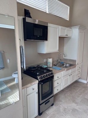 A compact kitchen with a stove, microwave, sink, and white cabinets.