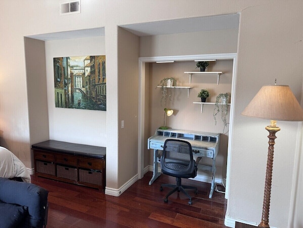 A compact room with a desk, chair, and a lamp. There is a bench and a painting on the wall.