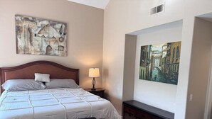 A bedroom with a large bed, a nightstand, a lamp, a bench, and two paintings on the wall. - Studio in QUIET  SFR home, gated community. (Laguna Niguel)