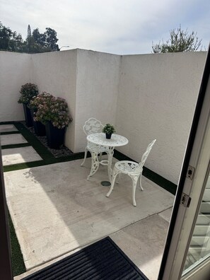 A patio with a white metal table and chairs, surrounded by potted plants and a small garden area.