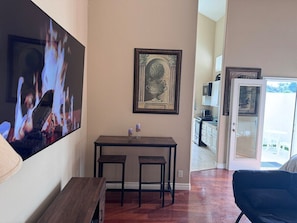 A dining area with a wooden table and two chairs, a framed artwork above the table, and a television displaying a fire scene.