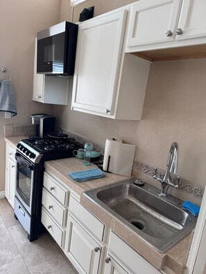 A compact kitchen with white cabinets, a stainless steel sink, and a black stove. - Studio in QUIET  SFR home, gated community. (Laguna Niguel)