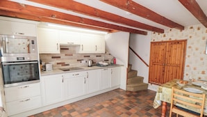 A kitchen with white cabinets, a microwave, an oven, and a sink. There's a staircase leading to a wooden door.