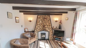 A cozy living room with a stone fireplace, a television, and striped carpeting.