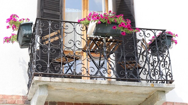 A balcony with wrought iron railings, a wooden door, and flower boxes with pink flowers.