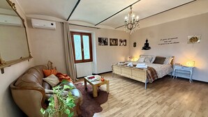A furnished room with a bed, a sofa, a coffee table, a potted plant, a chandelier, and a window with curtains.