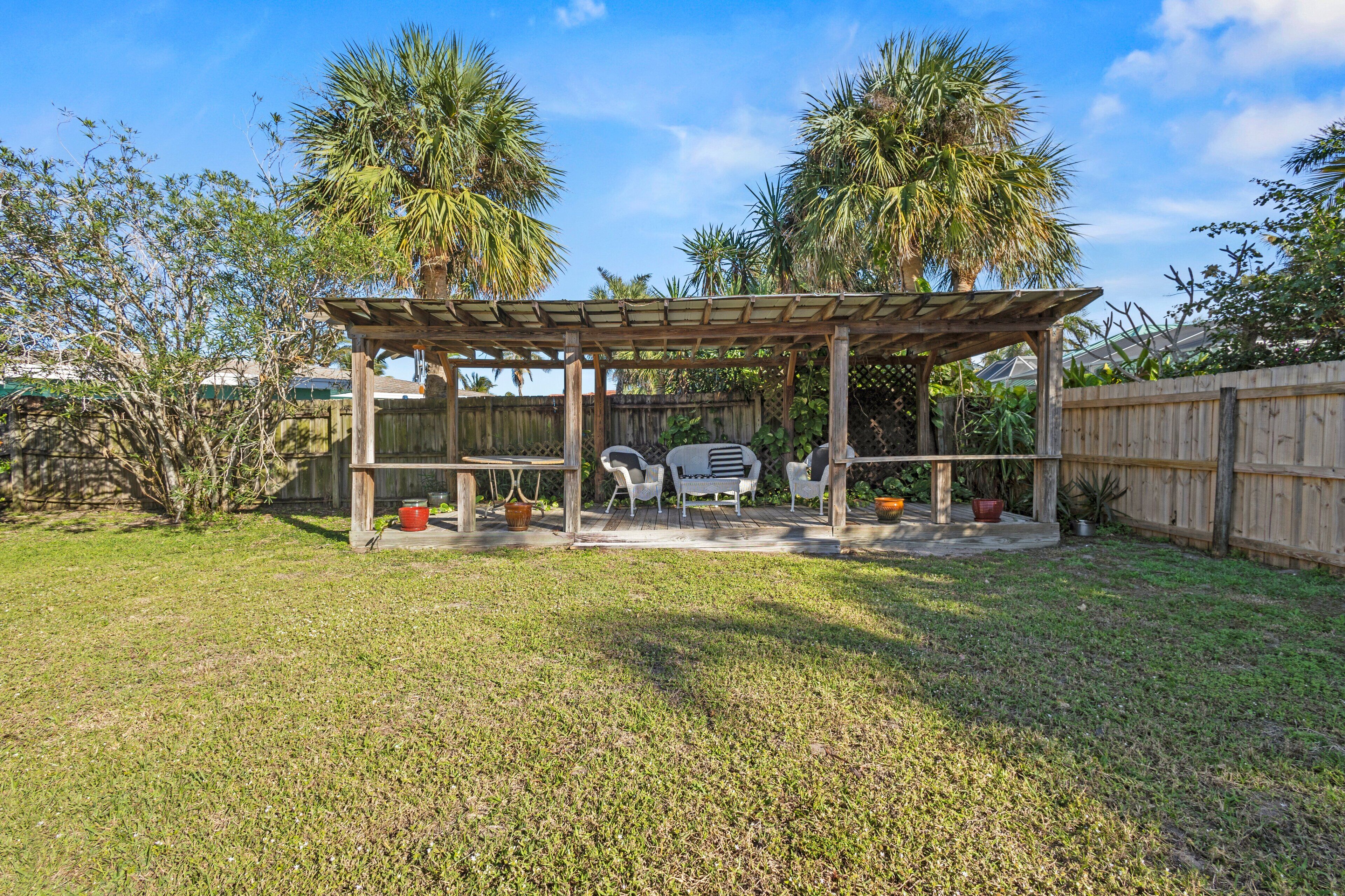 A wooden pergola with a table and chairs in a backyard.