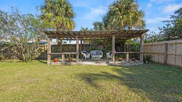 A wooden pergola with a table and chairs in a backyard.