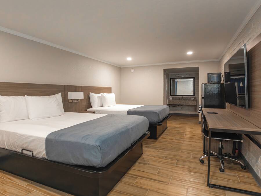 A hotel room with two beds, a desk, a television, and a small window.
