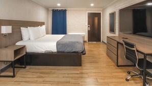 Ein modernes Hotelzimmer mit Bett, Schreibtisch, Sessel und einem großen Fernseher.