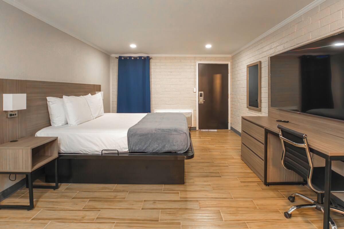 A modern hotel room with a bed, desk, chair, and a large TV.