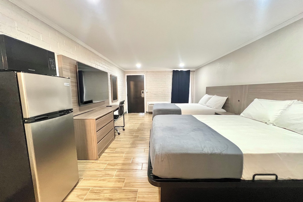 A modern hotel room with a kitchenette, a bed, a desk, and a television.