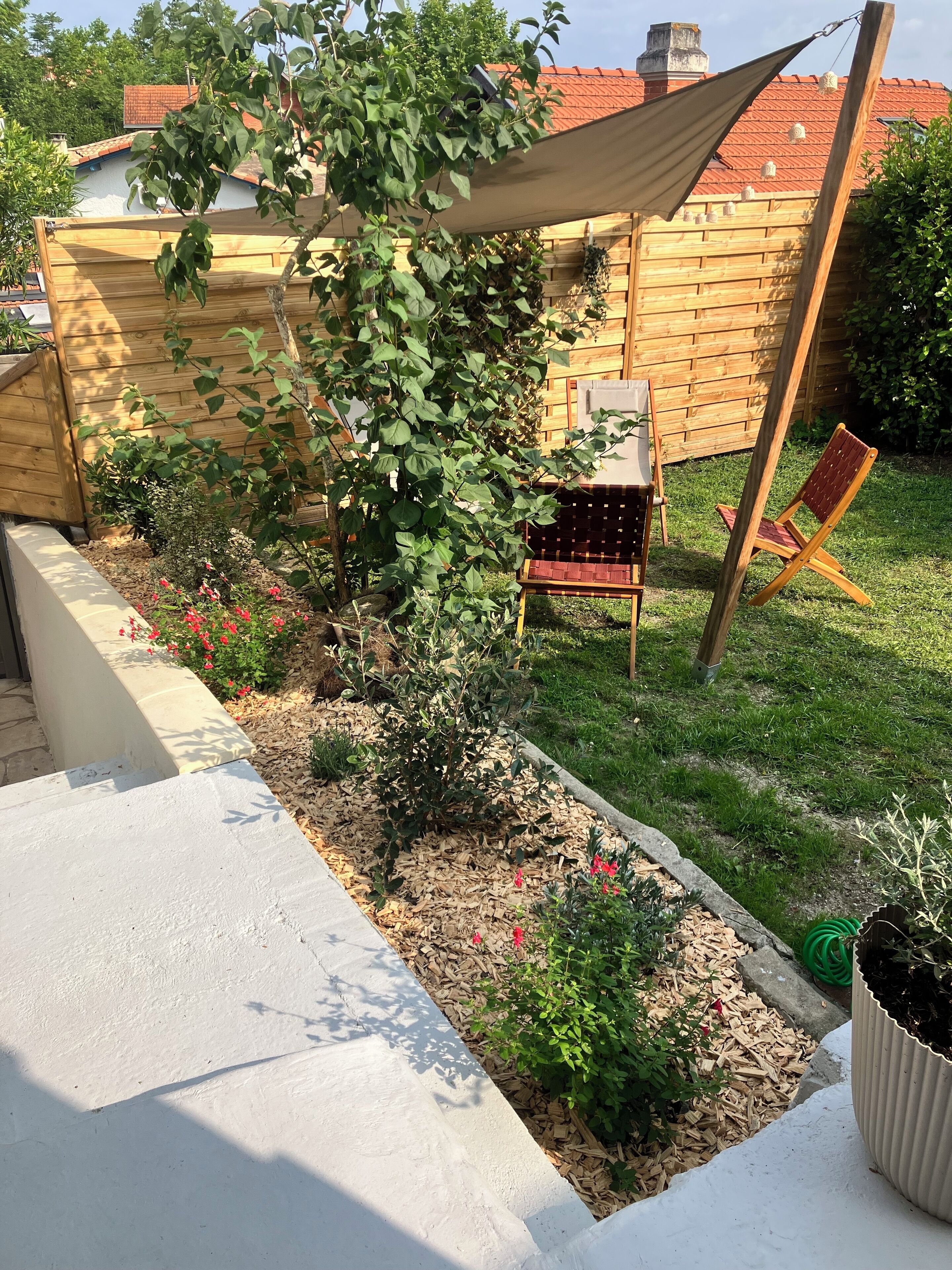 Un giardino con una recinzione in legno, una sedia di legno e un tavolino.