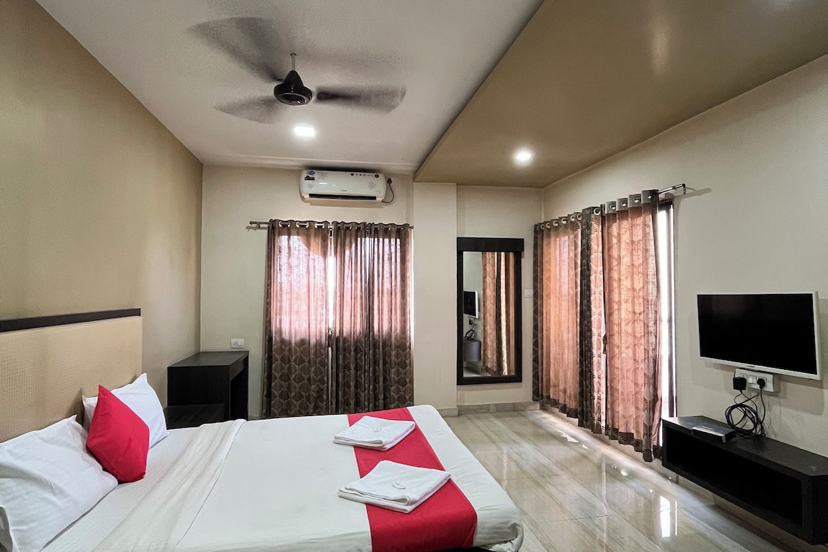 Une chambre d’hôtel avec un grand lit, un ventilateur de plafond, un appareil de climatisation, une télévision et une salle de bain visible à travers une porte.