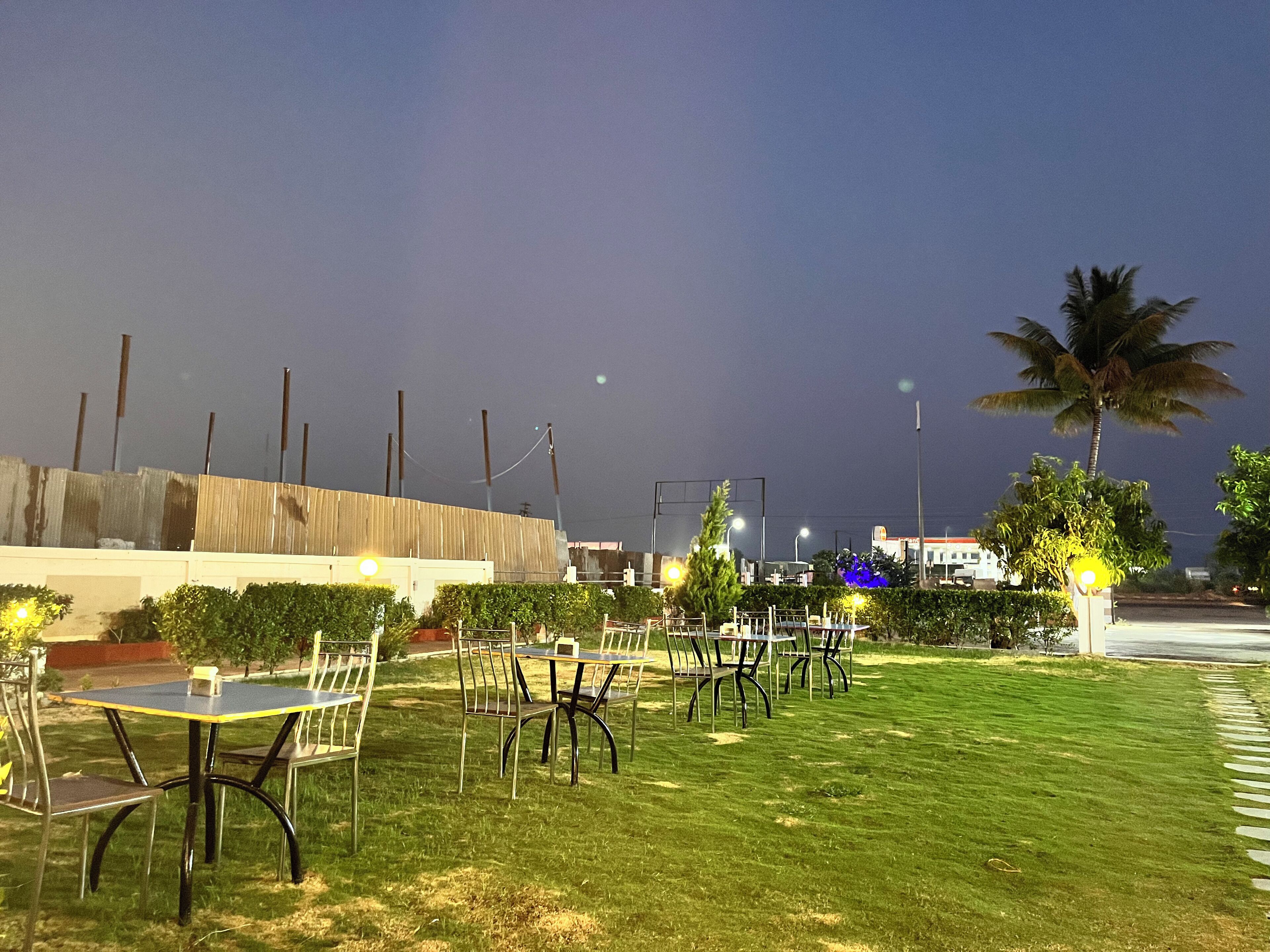 An outdoor seating area with tables and chairs, a grassy lawn, and a palm tree.