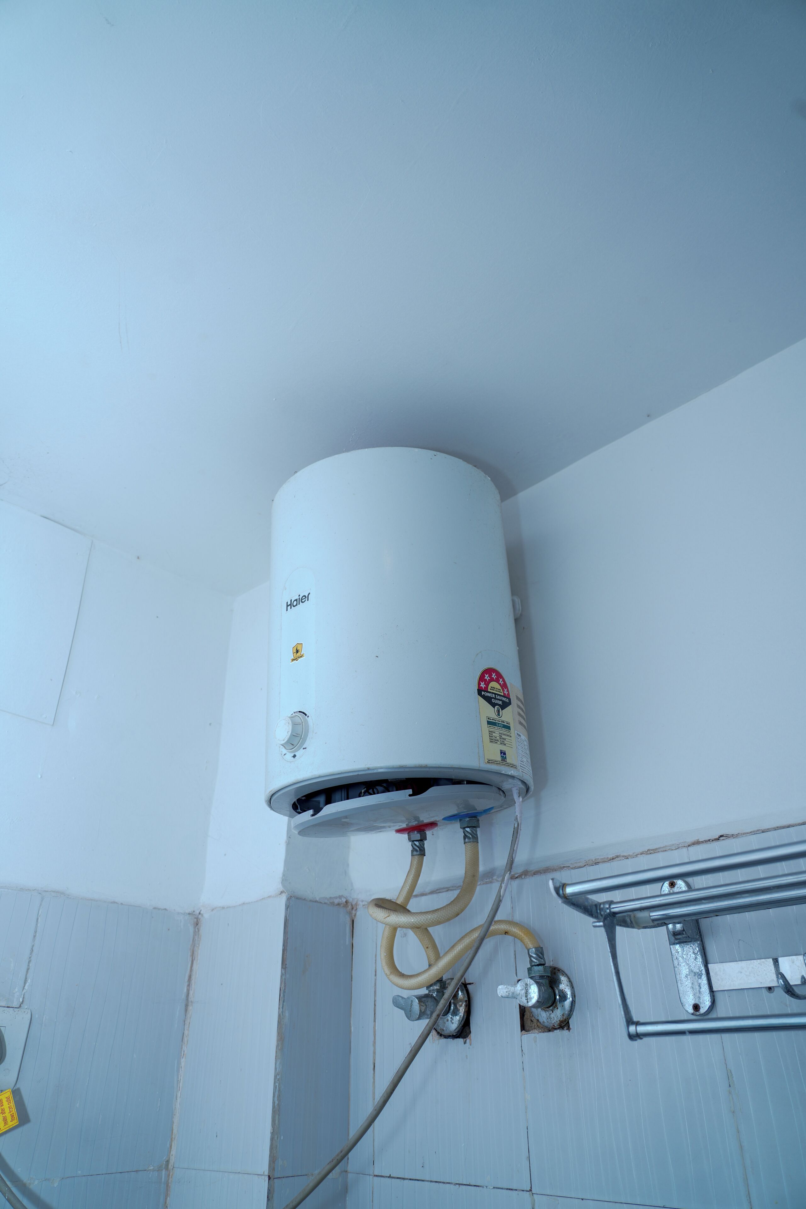 Un chauffe-eau blanc fixé au mur, avec des tuyaux apparents et un support métallique.