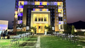 A hotel with a modern design, featuring a central entrance with a glass facade, surrounded by a well-maintained lawn and outdoor seating area. - Hotel Bhagyalaxmi  (Karad)