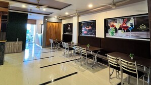 A hotel lobby with a reception desk, seating area, and a large screen displaying a beverage advertisement. - Hotel Bhagyalaxmi  (Karad)