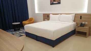 A hotel room with a bed, a bedside table with a phone, a chair, and a small table.