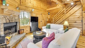 A cozy log cabin interior with a stone fireplace, white furniture, and a TV. - 3 Mi to Dtwn Clayton: Cabin w/ Trail Access! (Clayton)