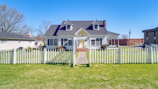 A two-story house with a white picket fence, a covered porch, and a clear blue sky. - 10 Mi to Caddo Lake: Charming Cottage in Vivian! (Vivian)