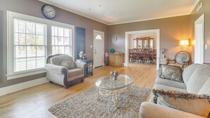 A living room with a ceiling fan, a clock, a dining area with a chandelier, and a fireplace. - 10 Mi to Caddo Lake: Charming Cottage in Vivian! (Vivian)