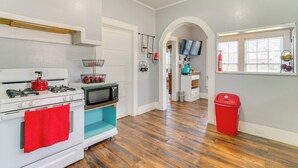 A kitchen with a stove, microwave, and oven, a red trash bin, and a window with blinds. - 10 Mi to Caddo Lake: Charming Cottage in Vivian! (Vivian)