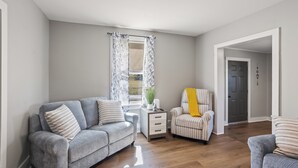 A living room with a grey sofa, a striped armchair, and a small table with a plant.