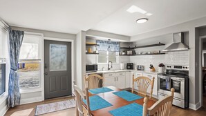 A modern kitchen with white cabinets, a stainless steel stove, and a dining area with blue placemats.