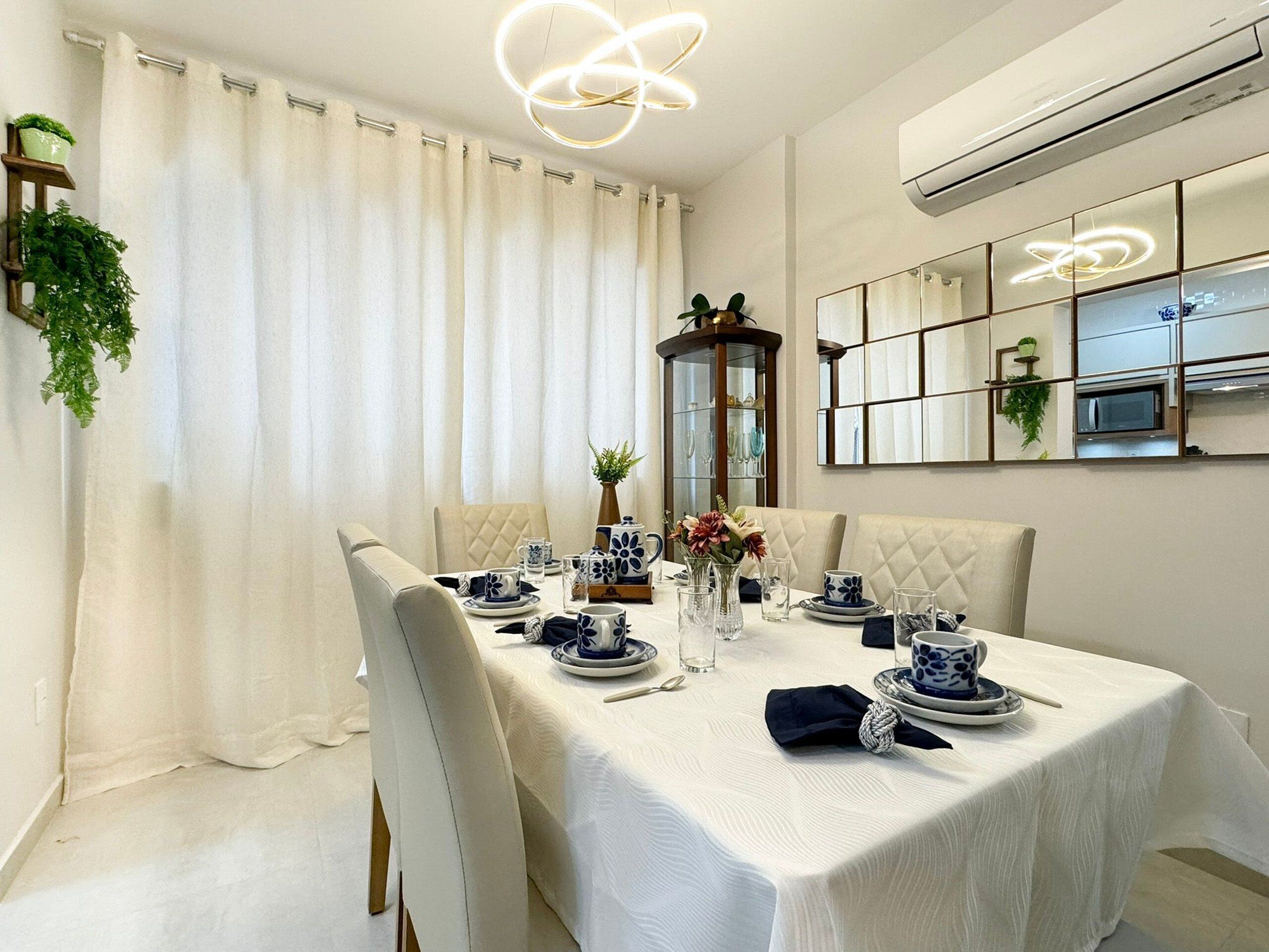 A dining area with a table set for four, featuring a white tablecloth, blue and white patterned tableware, and a vase with flowers.